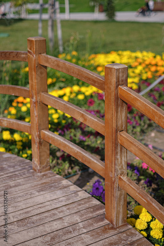 Mini bridge crossing in a green park. Summer time, green trees and colorful flowers.