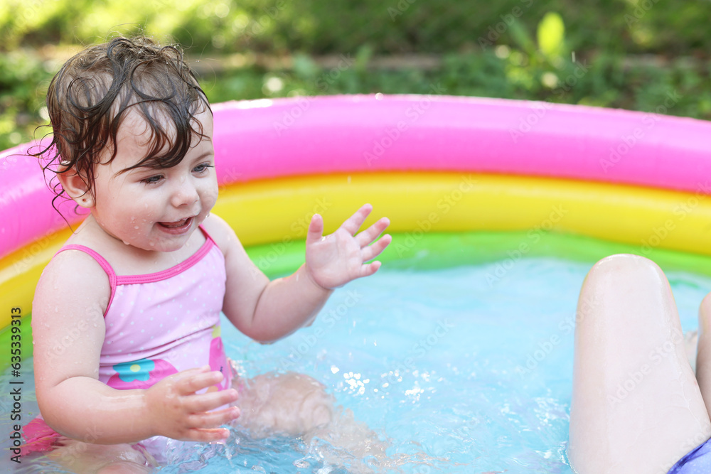 Children in the pool, it's hot in the summer. A little girl. A child plays in a children's pool. Swimming in the yard, inflatable pool in the shade. The girl loves water. Happy child in a swimsuit Children in the pool, it's hot in the summer. A little girl. A child plays in a children's pool. Swimming in the yard, inflatable pool in the shade. The girl loves water. Happy child in a swimsuit