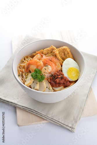 spicy nyonya noodlel malay laksa mee soup with seafood prawn, fish cake, egg, bean curd and chilli sambal thick gravy sauce in bowl on white background asian halal food cuisine menu for cafe design
