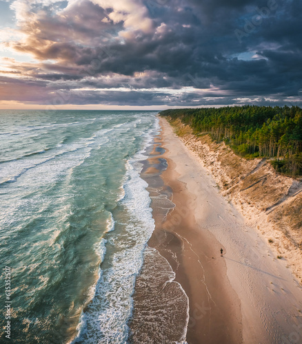 Baltic sea in colorful sunset colors with storm clouds. Turquoise water with waves, and sandy coastline.