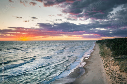 Fototapeta Naklejka Na Ścianę i Meble -  Baltic sea in colorful sunset colors with storm clouds. Turquoise water with waves, and sandy coastline.