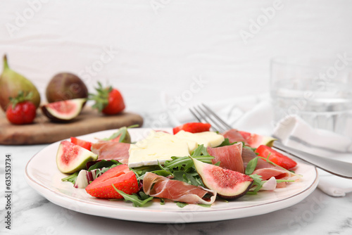 Tasty salad with brie cheese, prosciutto, strawberries and figs on white marble table
