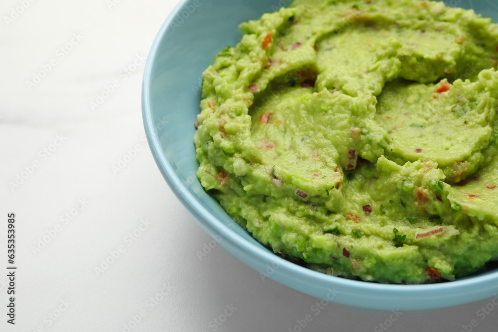 Bowl with delicious fresh guacamole on white table, closeup. Space for text