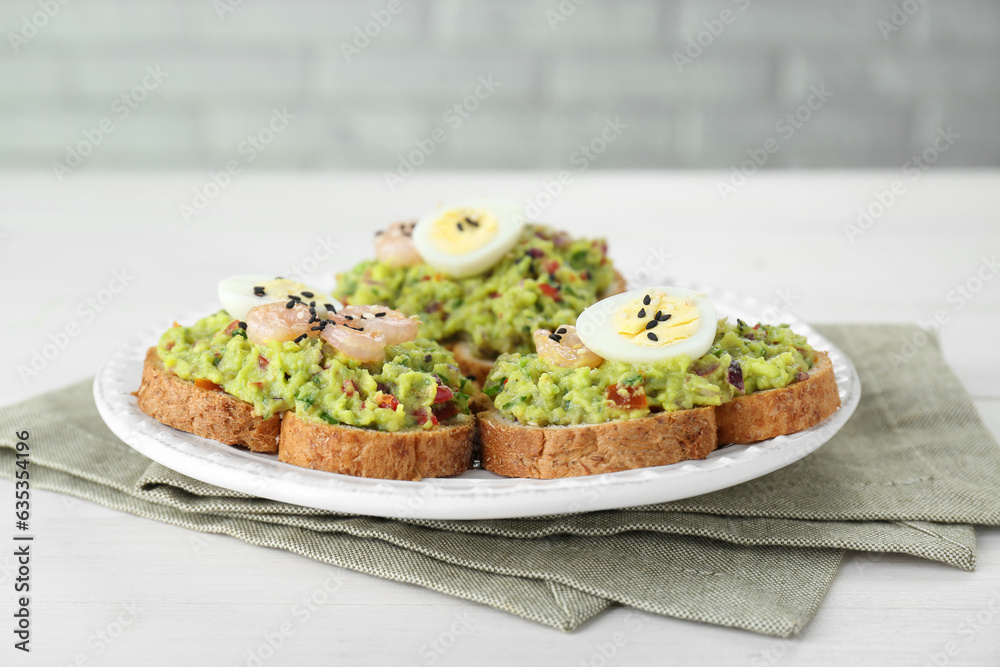 Slices of bread with tasty guacamole, eggs and shrimp on white wooden table, closeup Slices of bread with tasty guacamole, eggs and shrimp on white wooden table, closeup