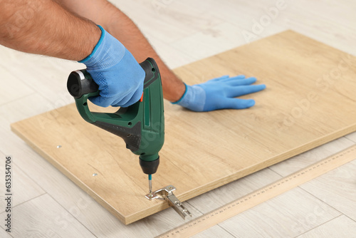Man with electric screwdriver assembling furniture on floor, closeup