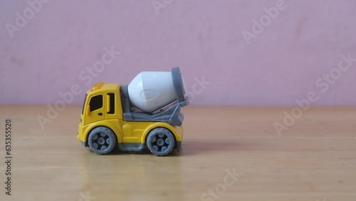 Industrial mechanical yellow cement truck toy drive on wooden table, plaything for kid learning about construction site work and logistic work, copy space