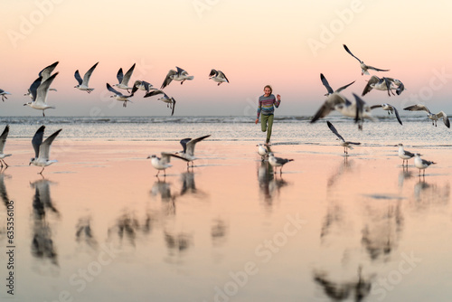 Girl running on beach with seagulls at sunset photo