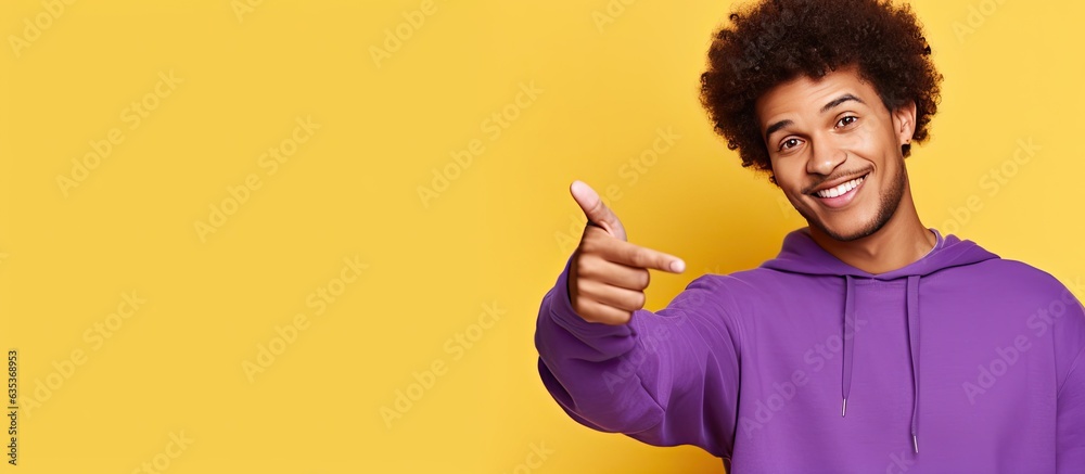 African American man in purple hoodie posing happily pointing to empty space for ad African American man in purple hoodie posing happily pointing to empty space for ad