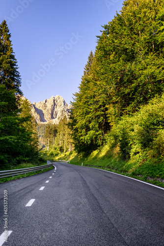 Italian Alpine road running trough a forest with Siera mount in background. Road to Sappada, Udine province, Friuli Venezia Giulia, Italy. photo