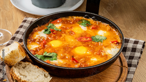 Traditional oriental cuisine. Arabic dish Shakshuka. Turkish breakfast, fried eggs, tomato sauce, peppers, cilantro and 2 pieces of baguette.