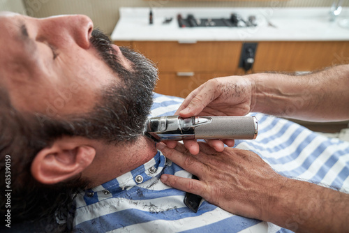 Professional hairdresser trimming beard of male hipster