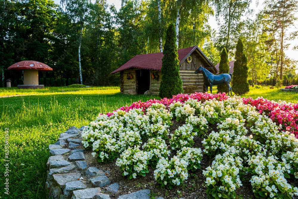 Park z drzewami liściastymi, pięknymi trawnikami, klombami kolorowych kwiatów i alejkami. Lato na Śląsku w Polsce, Rogów gmina Gorzyce.