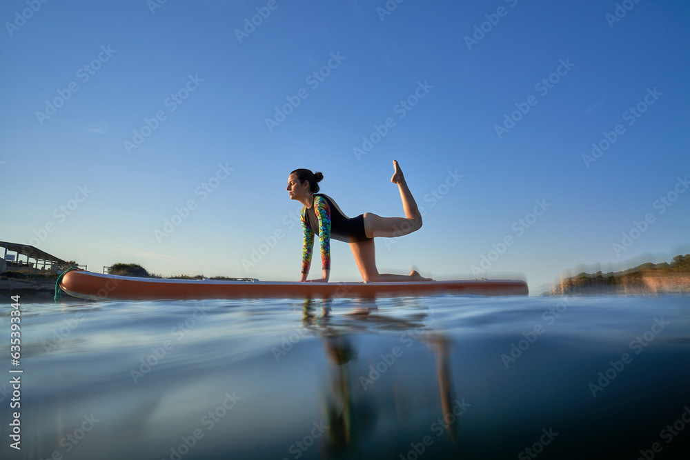 Sportswoman taking Tiger pose on paddleboard in sea