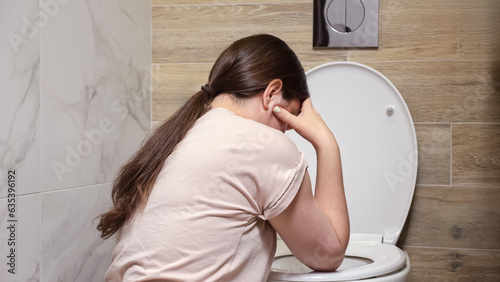 Woman feels nauseous sitting near toilet in bathroom. Feeling unwell after spending time at party. Consequences of drinking alcohol backside view photo