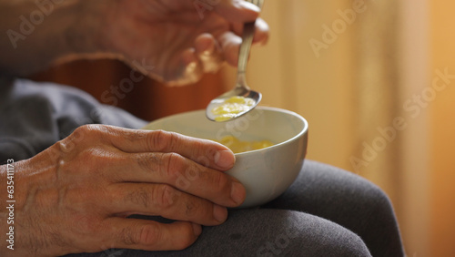 The older man's hands hold the bowl in his lap during breakfast.