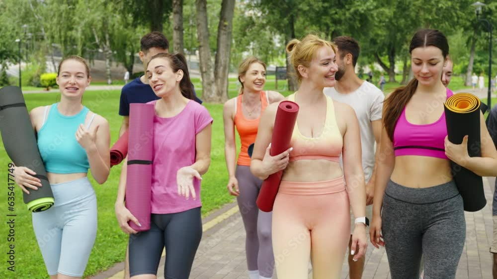 Cheerful group of young people with mats heading to the park for fitness session. Good mood before yoga training. Outdoor sports activities in the fresh air. Health and wellness concept Cheerful group of young people with mats heading to the park for fitness session. Good mood before yoga training. Outdoor sports activities in the fresh air. Health and wellness concept