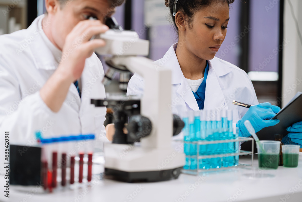 Team of biochemical research scientists working with a microscope for vaccine development in pharmaceutical research labeling. Team of biochemical research scientists working with a microscope for vaccine development in pharmaceutical research labeling.