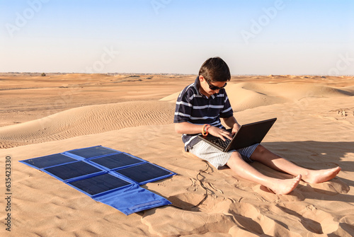 Teen (young boy) with his laptop in the desert connected to solar panel