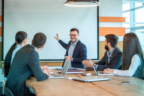 Male presenter giving business presentation on white board at briefing in conference room.