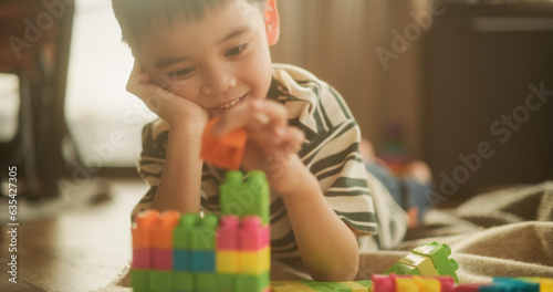 Portrait of Male Asian Kid Playing with Colorful Building Blocks in his Room During the Day. Cute Little Creative Child Focused on Making a Toy House. Concept of Nostalgia, Childhood and Innocence