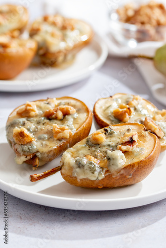 Baked pears with blue cheese, walnuts and honey on white plate and light background