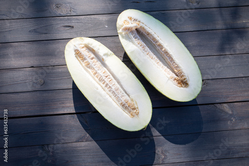 Two halves of a melon on a wooden table, melon seeds in the middle