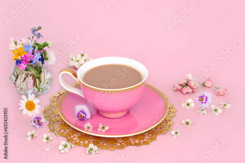 Afternoon tea with Spring flowers and wildflowers in a vase and scattered. Luxury tea cup on gold doily on pink background.