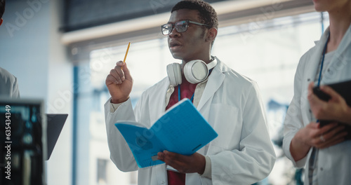 Portrait of a Young Black Male Engineering Student Asking Questions and Taking Notes in a Laboratory. Lab Assistant in a Meeting Showing Initiative and Giving Ideas, Brainstorming with his Team