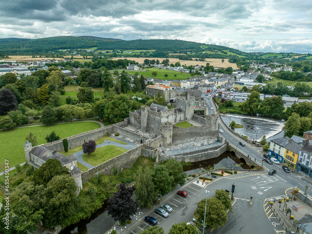 Aerial view of Cahir castle and town in Ireland with Tower House, outer castle, circular, rectangular towers, banquette hall, guarding the crossing on the River Suir with a waterfall and golf course