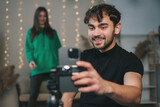 Boy turning on the phone camera to film a video blog together with his girlfriend, spending free time at home. Concept of video blogging and social networks