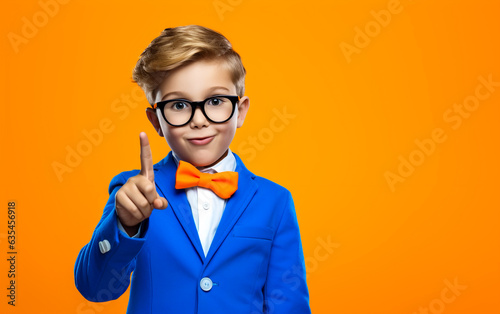 The smiling little child points up in front of him - isolated on orange background