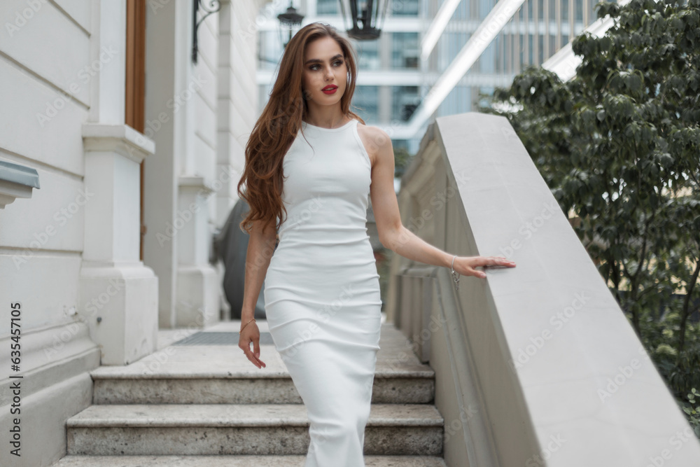 Elegant beautiful vogue girl model in a fashion white dress goes down the stairs near the vintage building. Pretty chic lady. Brunet glamours woman Elegant beautiful vogue girl model in a fashion white dress goes down the stairs near the vintage building. Pretty chic lady. Brunet glamours woman