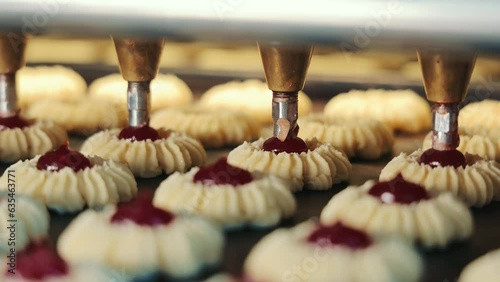 Process of adding Berry Jam to freshly baked Cookies in Confectionery Factory. Close up of Biscuits being filled with Jam and transported on Conveyor Belt. Concept of Automated Technology Equipment