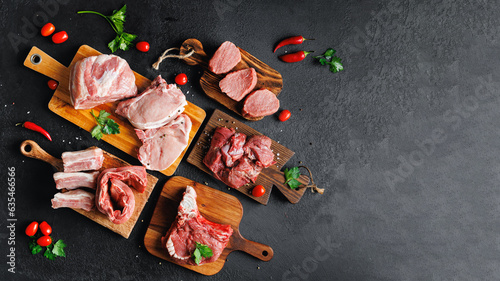 Variety of raw beef meat and pork ribs, pig steaks for grilling with seasoning on wooden board, dark rustic background copy space
