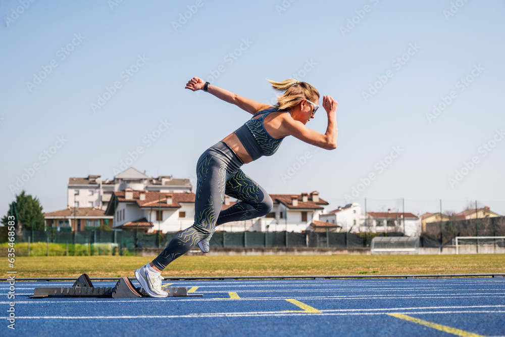 Woman ready to sprint start in athletics - Sprinter girl in starting blocks ready for the race on the track - obrazy, fototapety, plakaty 