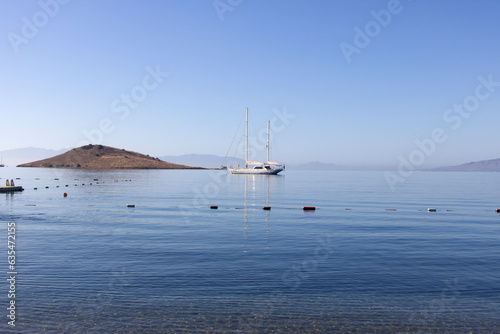 A single white sailing boat in blue aegean sea with mountain and sky in background, with copy space.