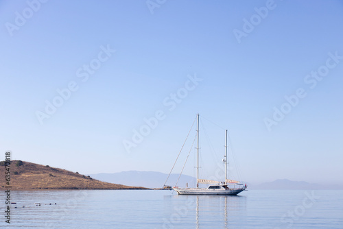 A single white sailing boat in blue aegean sea with mountain and sky in background, with copy space.