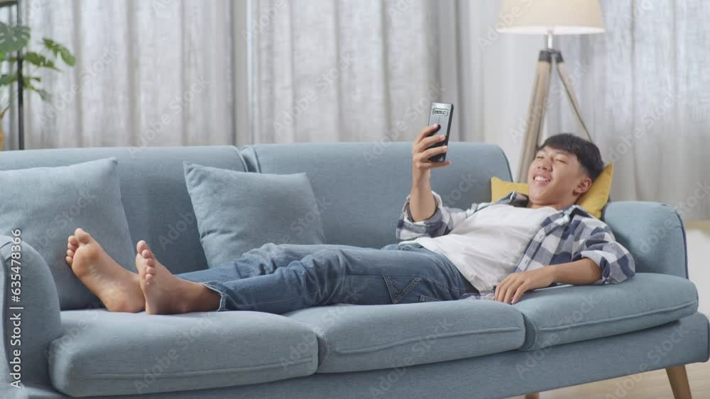 Full Body Of Asian Teen Boy Having Video Call On Smartphone While Lying On Sofa In The Living Room At Home. Waving Hands, Smiling, And Speaking
Full Body Of Asian Teen Boy Having Video Call On Smartphone While Lying On Sofa In The Living Room At Home. Waving Hands, Smiling, And Speaking