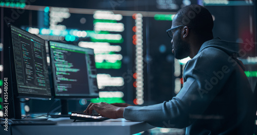 Black Male Programmer Working in Monitoring Room, Surrounded by Big Screens Displaying Lines of Programming Language Code. Portrait of Man Creating a Software. Abstract Futuristic Coding Concept