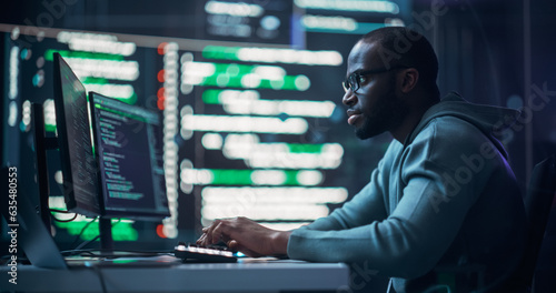 Focused Black Male Programmer Working in Monitoring Room, Surrounded by Big Screens Displaying Lines of Programming Language Code. Portrait of Man Creating Software. Futuristic Coding Concept.