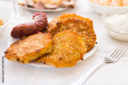 Potato pancakes with fried sausage on white plate