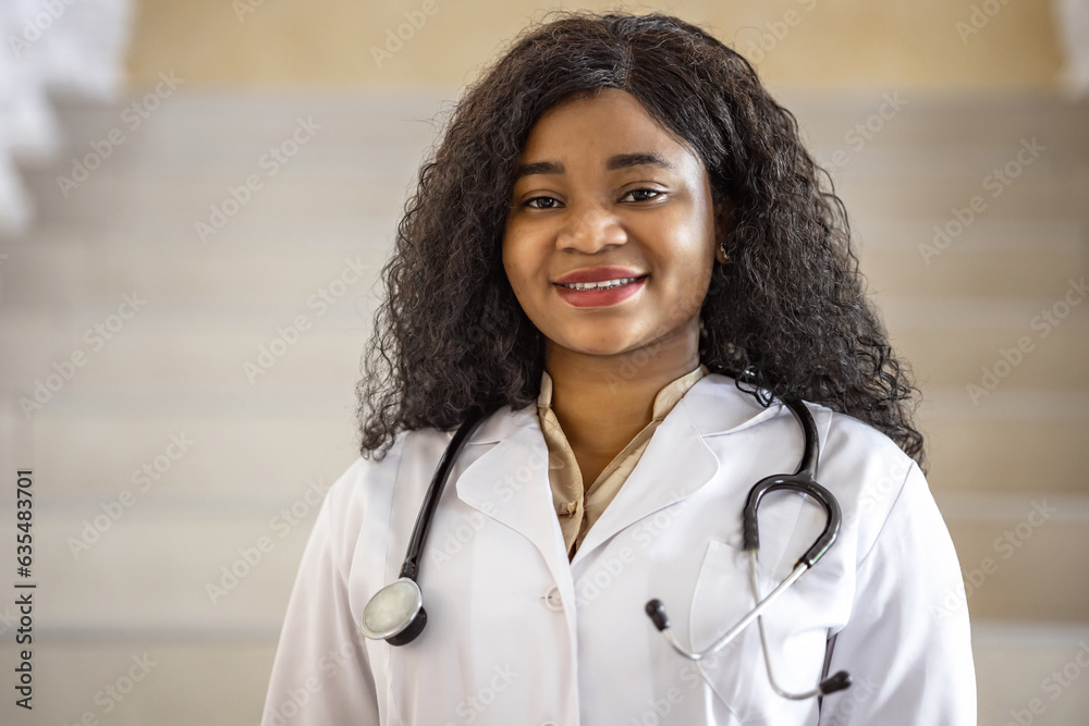 Portrait of smiling positive African ethnicity female medic in medical white coat standing and looking directly at the camera at the clinic. Concept: health, medical clinic, insurance Portrait of smiling positive African ethnicity female medic in medical white coat standing and looking directly at the camera at the clinic. Concept: health, medical clinic, insurance