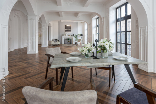 a view of a set dining table in a chic expensive bright interior of a huge living room in a historic mansion with arched arches, columns and white walls decorated with ornaments and stucco. © 4595886