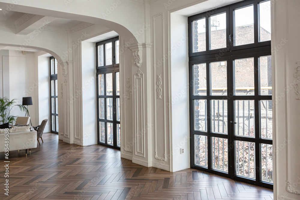Fototapeta premium a chic expensive bright interior of a huge living room in a historic mansion with arched arches, columns and white walls decorated with ornaments and stucco.