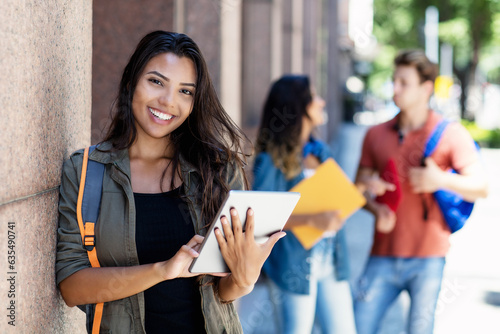 Laughing mexican student with tablet computer and friends in background in front of university building