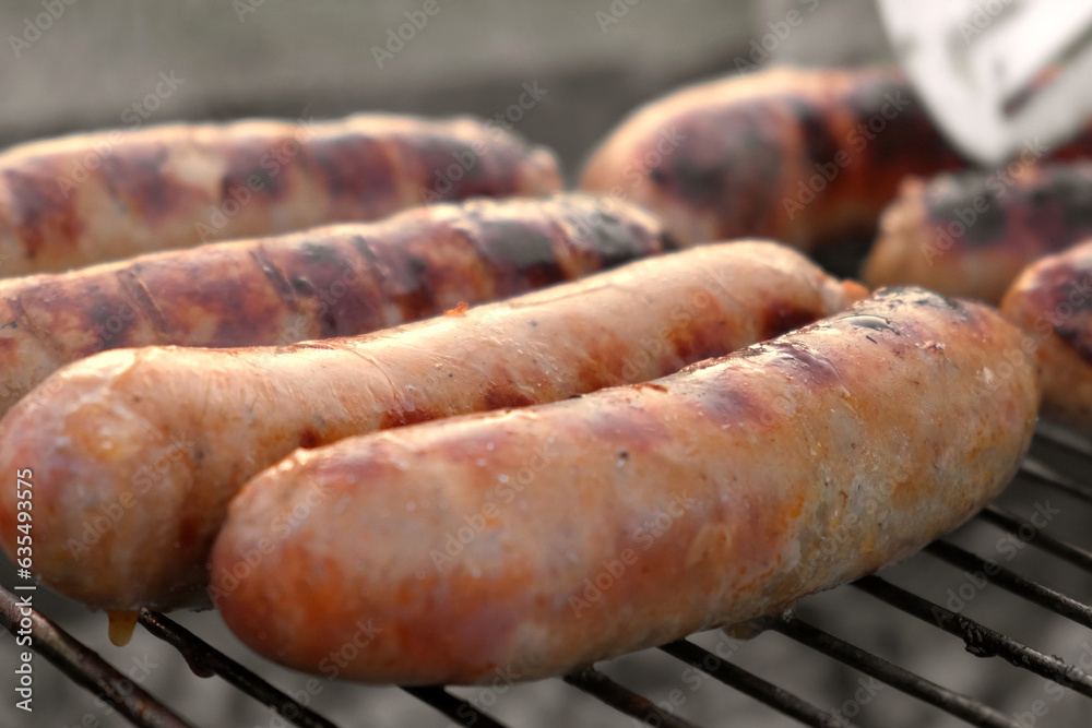 Grilled sausages. Cook man preparing grilling food bbq. Barbecue with smoke, flame outdoors. Tasty juicy german bratwurst. Charcoal kettle grill outside in backyard. Family summer vacation. Close-up	
