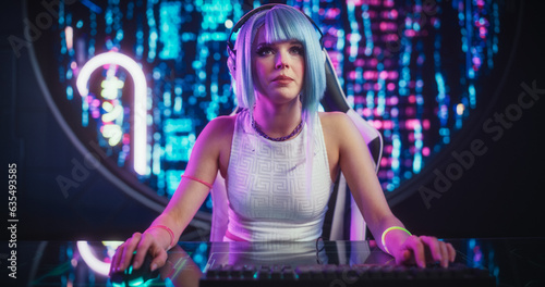Attractive Cosplay Girl Playing Internet Video Game with Other Players on Desktop Computer While Sitting in Futuristic Cyberpunk Home. Young Female Talking to Her Online Friends © Gorodenkoff