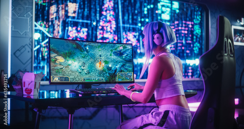 Young Female Gamer Playing Strategy Video Game with Modern Graphics on Her Computer. Stylish Futuristic Cyberpunk Gaming Neon Room with Cosplay Gamer Girl in Headphones. Photo from the Back