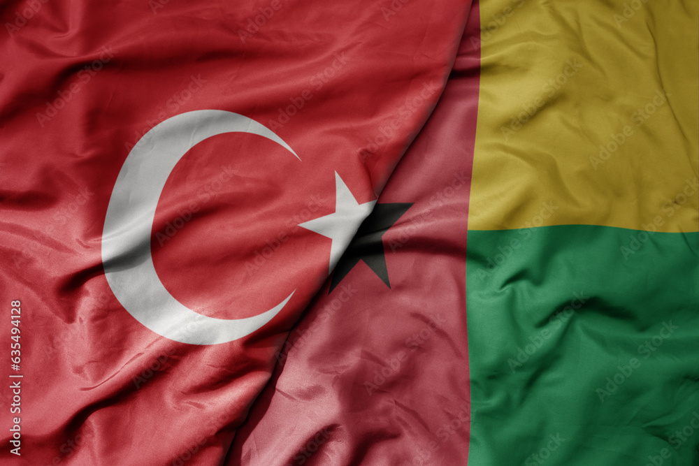 big waving national colorful flag of turkey and national flag of guinea bissau .