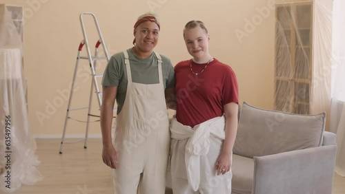 Medium portrait of young multiracial lesbian couple in coveralls posing for camera in renovating apartmentMedium portrait of young multiracial lesbian couple in coveralls posing for camera in renovati photo